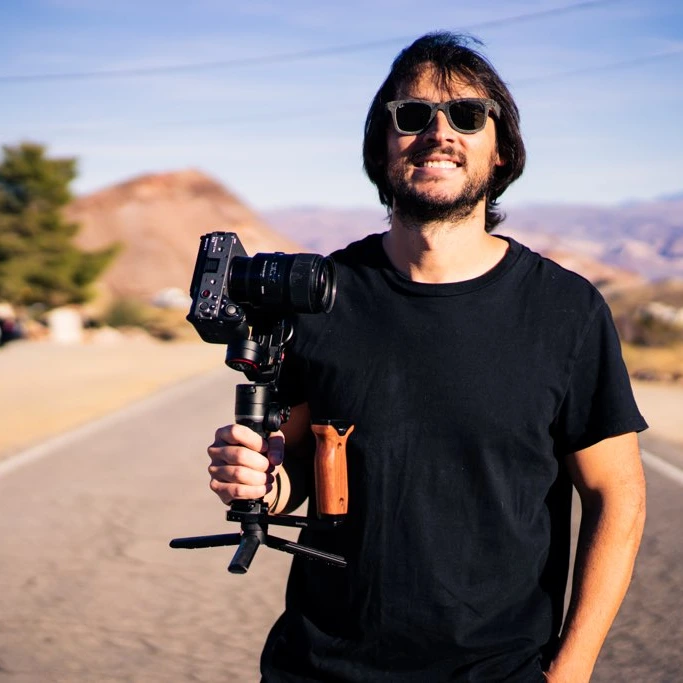 Tiago Fantin smiling, holding his camera on a gimbal on a desert road